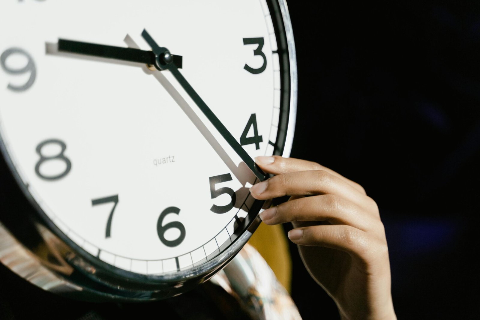 Home A hand adjusting the time on a large analog clock with bold numbers.